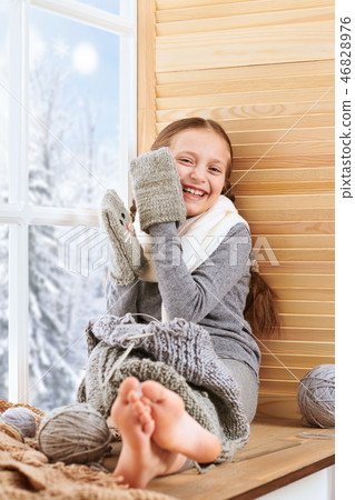 Child girl is sitting on window sill and knitting 46828976