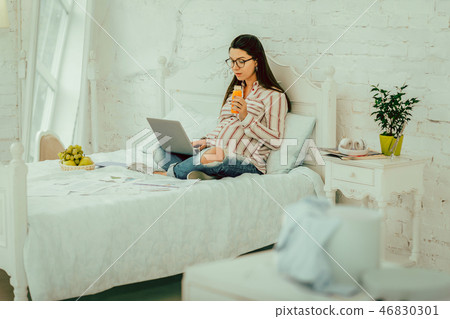 Pregnant woman drinking a juice and working remotely 46830301