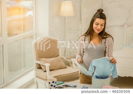 Smiling pregnant woman unpacking new children clothes 46830309