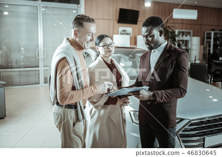 Cheerful businessman wearing orange turtle neck signing documents 46830645