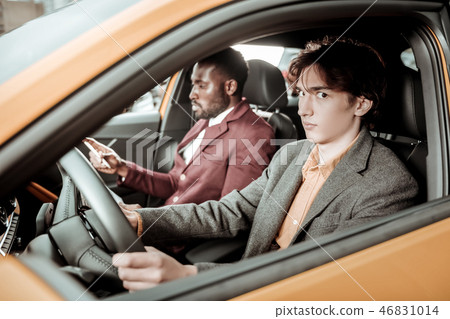 Dark-eyed young man feeling nervous while driving for the first time Dark-eyed young man feeling nervous while driving for the first time 46831014