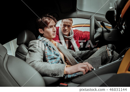 Young handsome son sitting behind the wheel while choosing car Young handsome son sitting behind the wheel while choosing car 46831144