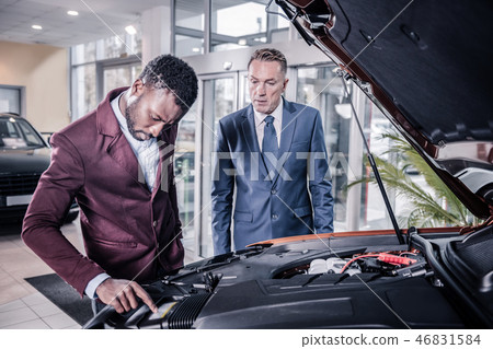 Sales manager of car salon opening front trunk describing car for client Sales manager of car salon opening front trunk describing car for client 46831584