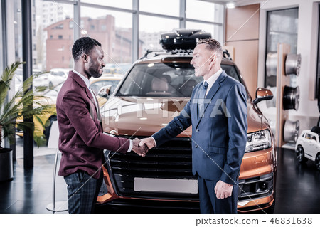 Businessman in dark suit shaking hand of sales manager in car salon Businessman in dark suit shaking hand of sales manager in car salon 46831638