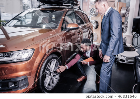 Sales manager of car salon telling his client about the wheels Sales manager of car salon telling his client about the wheels 46831646