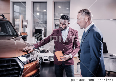 Consultant of car salon telling about the advantages of new car Consultant of car salon telling about the advantages of new car 46831663