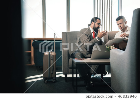 Two business partners sitting on sofa in hotel lobby near their luggage 46832940