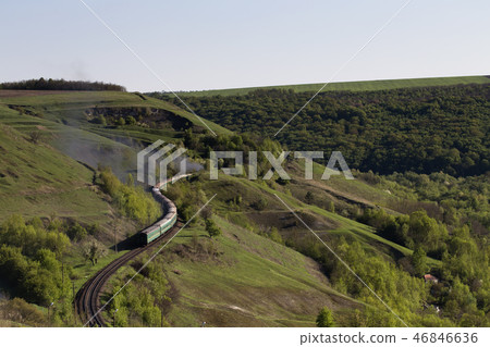 The train is going between green hills. The train is going between green hills. 46846636