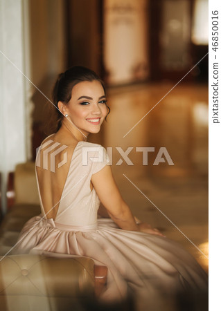 Beautiful stunning young lady in amazing dress sitting on luxury armchair 46850016