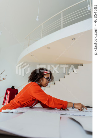 Dark-skinned busy woman leaning on her work table Dark-skinned busy woman leaning on her work table 46854583
