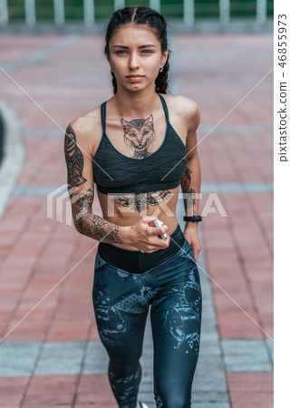 The girl in sportswear. In his hand smartphone. Runs on jogging, in the morning in the summer in the The girl in sportswear. In his hand smartphone. Runs on jogging, in the morning in the summer in the 46855973