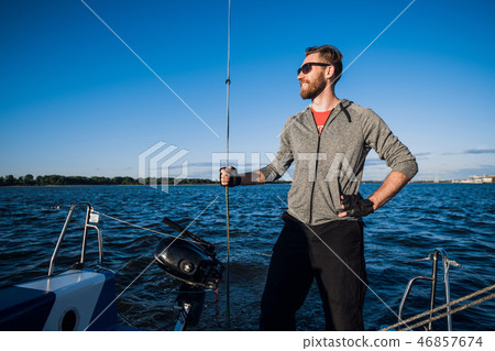 Young man wearing sunglasses standing on yacht stern and enjoying perfect autumn day under sails - 46857674