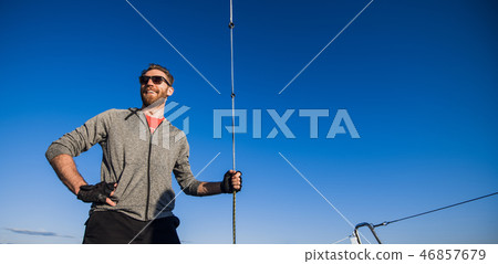 Young man wearing sunglasses standing on yacht stern and enjoying perfect autumn day under sails - 46857679