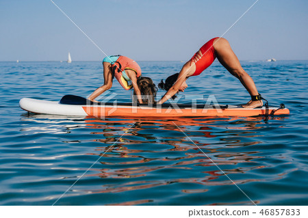 Mom and little daughter doing yoga on the paddle board Mom and little daughter doing yoga on the paddle board 46857833