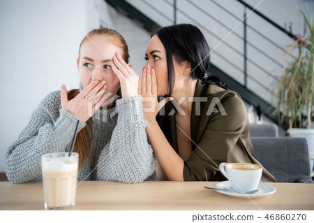 Pretty woman whispering secret to her curious friend. Young woman telling gossip to amazed female 46860270