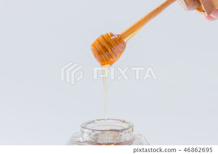 Honey drips from a wooden honey dipper on a white background Honey drips from a wooden honey dipper on a white background 46862695