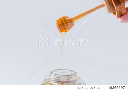 Honey drips from a wooden honey dipper on a white background Honey drips from a wooden honey dipper on a white background 46862697
