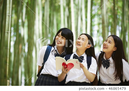 Three high school girls opening guidebook in bamboo forest 46865479