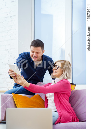 Friends sit on the couch, chatting and using a tablet computer. 46873644