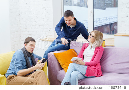 Friends sit on the couch, chatting and using a smartphone, desktop computer, laptop. Friends sit on the couch, chatting and using a smartphone, desktop computer, laptop. 46873646