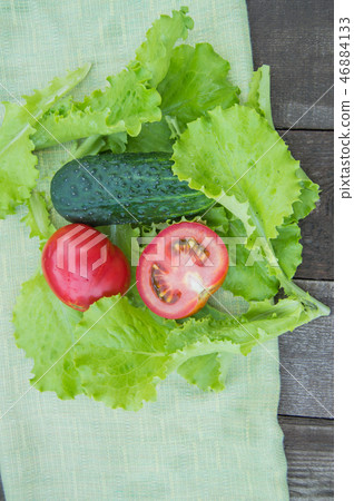 Sliced cucumbers and tomatoes lie on a green napkin, next to lettuce leaves, old dark wooden Sliced cucumbers and tomatoes lie on a green napkin, next to lettuce leaves, old dark wooden 46884133