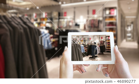 Woman hands taking a tablet in shopping mall with blurred image of clothes shop. 46890277