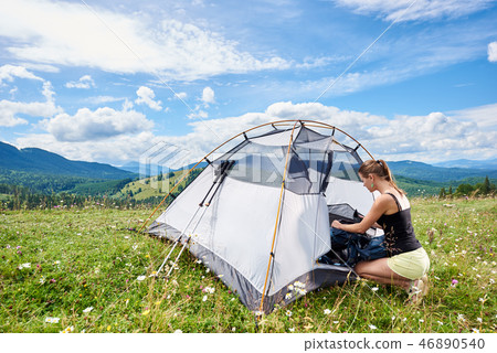 Woman tourist hiking in mountain trail, enjoying summer sunny morning in mountains near tent Woman tourist hiking in mountain trail, enjoying summer sunny morning in mountains near tent 46890540