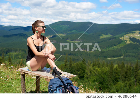 Woman hiker hiking on grassy hill, wearing backpack, using trekking sticks in the mountains 46890544