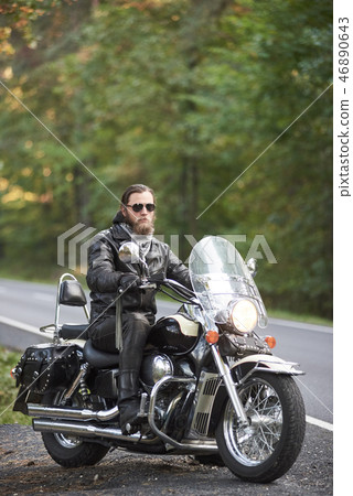 Bearded biker in black leather jacket on modern motorcycle on country roadside. Bearded biker in black leather jacket on modern motorcycle on country roadside. 46890643