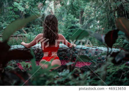 Attractive slim girl is standing back in the jungle. Brunette model in in the pool of flowers. Spa 46913650