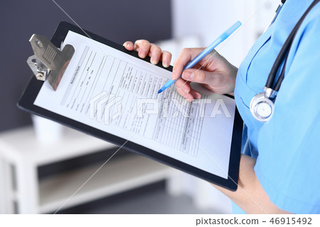 Female doctor filling up medical form on a clipboard, closeup. Healthcare, insurance and medicine Female doctor filling up medical form on a clipboard, closeup. Healthcare, insurance and medicine 46915492