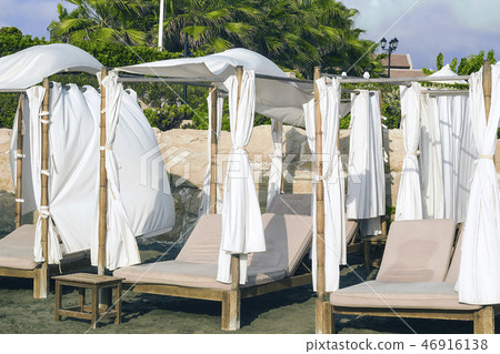 Wooden sunbeds with drapes on sandy beach 46916138