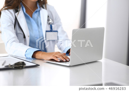 Unknown doctor woman typing on laptop computer while sitting at the desk in hospital office. close 46916283