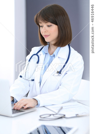 Doctor typing on laptop computer while sitting at the white table in hospital office. Physician at Doctor typing on laptop computer while sitting at the white table in hospital office. Physician at 46916446