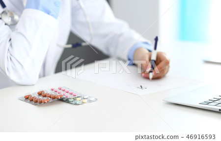 Female doctor filling up prescription form while sitting at the desk in hospital closeup.  Healthcar 46916593