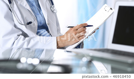 Female doctor filling up medical form on clipboard, closeup. Reflecting glass table is a physician Female doctor filling up medical form on clipboard, closeup. Reflecting glass table is a physician 46918450