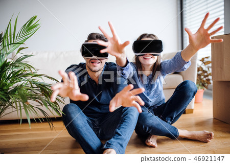 A young couple with VR goggles sitting on a floor, moving in a new home. A young couple with VR goggles sitting on a floor, moving in a new home. 46921147
