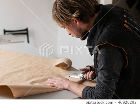 Young man tailor with scissors making clothing pattern Young man tailor with scissors making clothing pattern 46926292