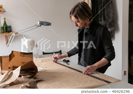 Young creative man tailor draws clothing pattern in workshop Young creative man tailor draws clothing pattern in workshop 46926296