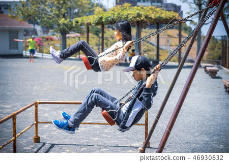 Brother and sister playing on the park swing 46930832