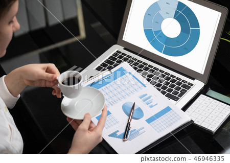 Businesswoman holding mug of coffee and acquainted with diagrams 46946335