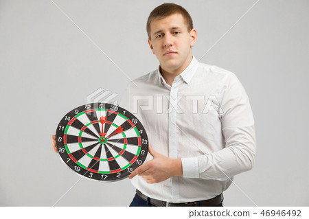 young man in white shirt holding a target with Darts in center isolated on white background 46946492