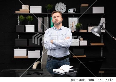 young man stands near the computer table and folded his hands on his chest 46946512
