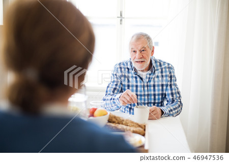 A senior couple sitting at the table at home, having breakfast. A senior couple sitting at the table at home, having breakfast. 46947536