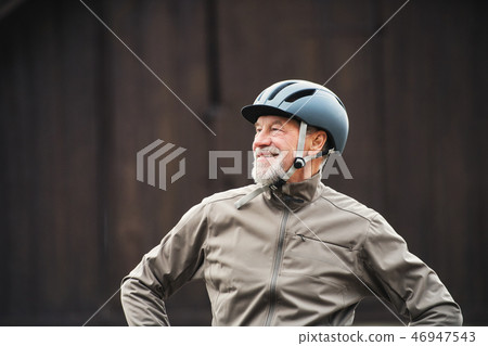 Active senior man with bike helmet standing outdoors againts dark background. 46947543