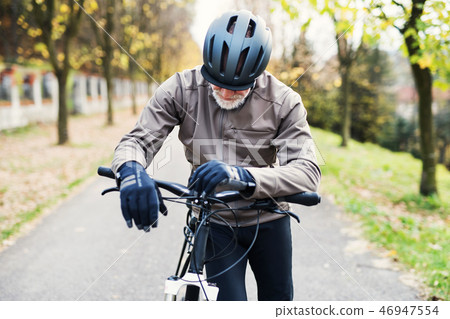 Active senior man with electrobike standing outdoors on a road in nature. 46947554