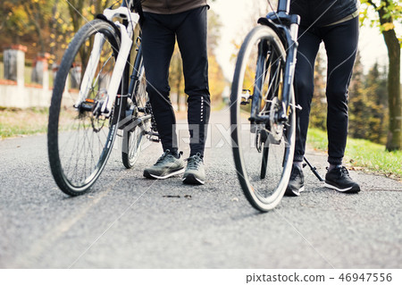 Legs and feet of couple with electrobikes outdoors on a road in park. Legs and feet of couple with electrobikes outdoors on a road in park. 46947556
