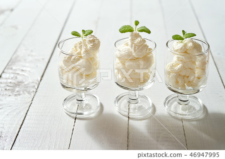 Glasses with a dessert of whipped cream with a fresh mint leaf on a white wooden table. 46947995