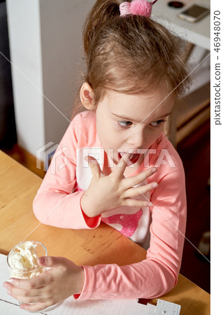 Pretty little girl holding dessert of whipped cream and raspberries and mint at wooden table. 46948070