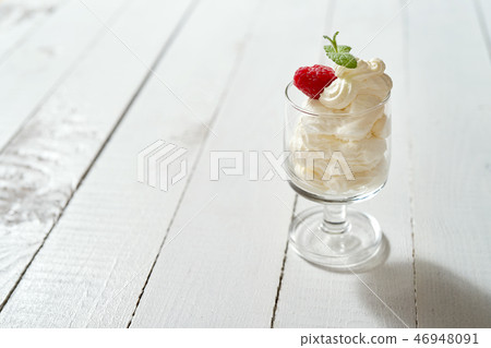 Glass of dessert with whipped cream with a fresh mint leaf and raspberry on white table. 46948091